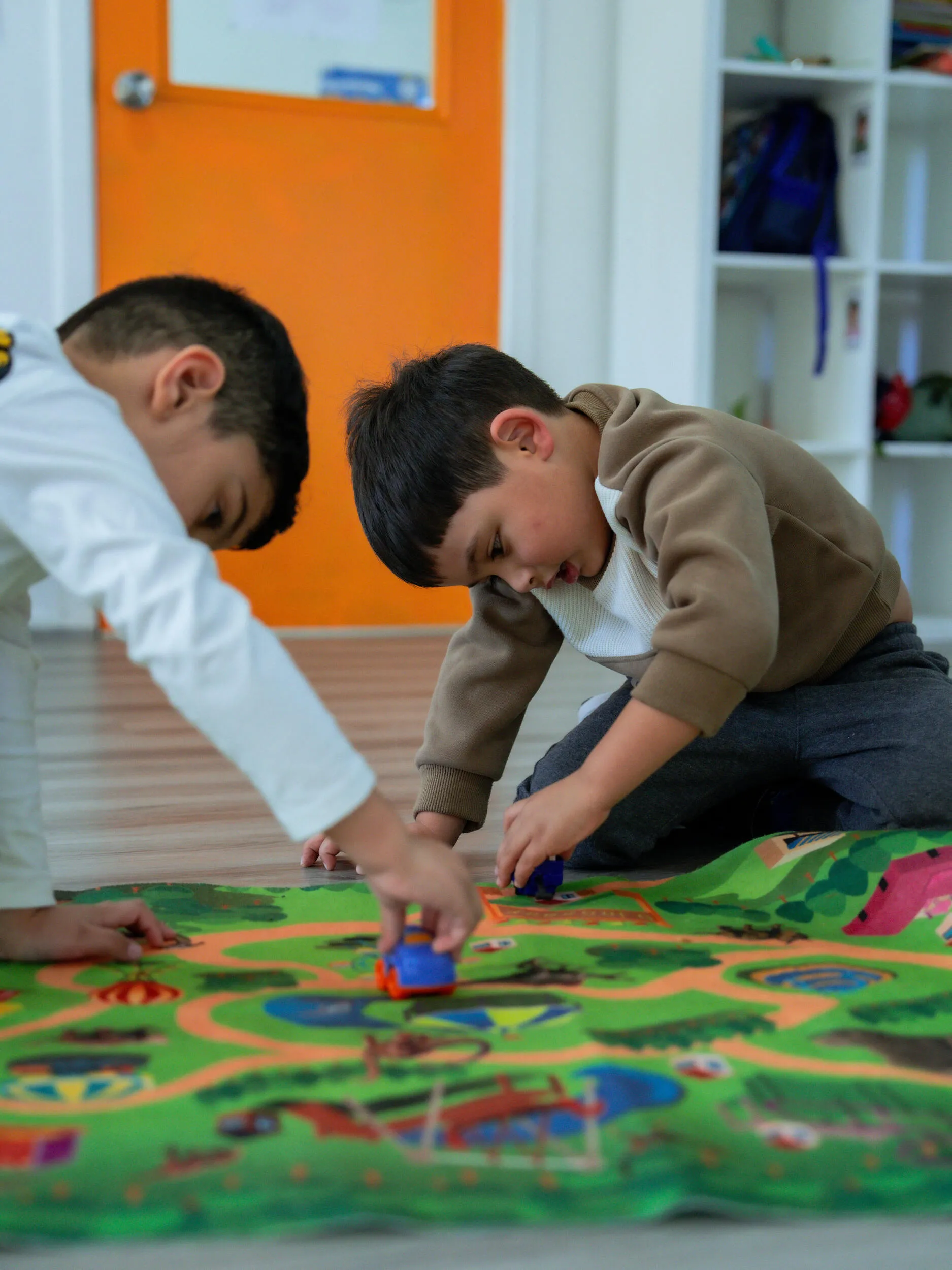 Kinderworld Early Learning Centre toddlers playing with toy cars on colourful road-themed activity mat during floor time applying Play-Based learning