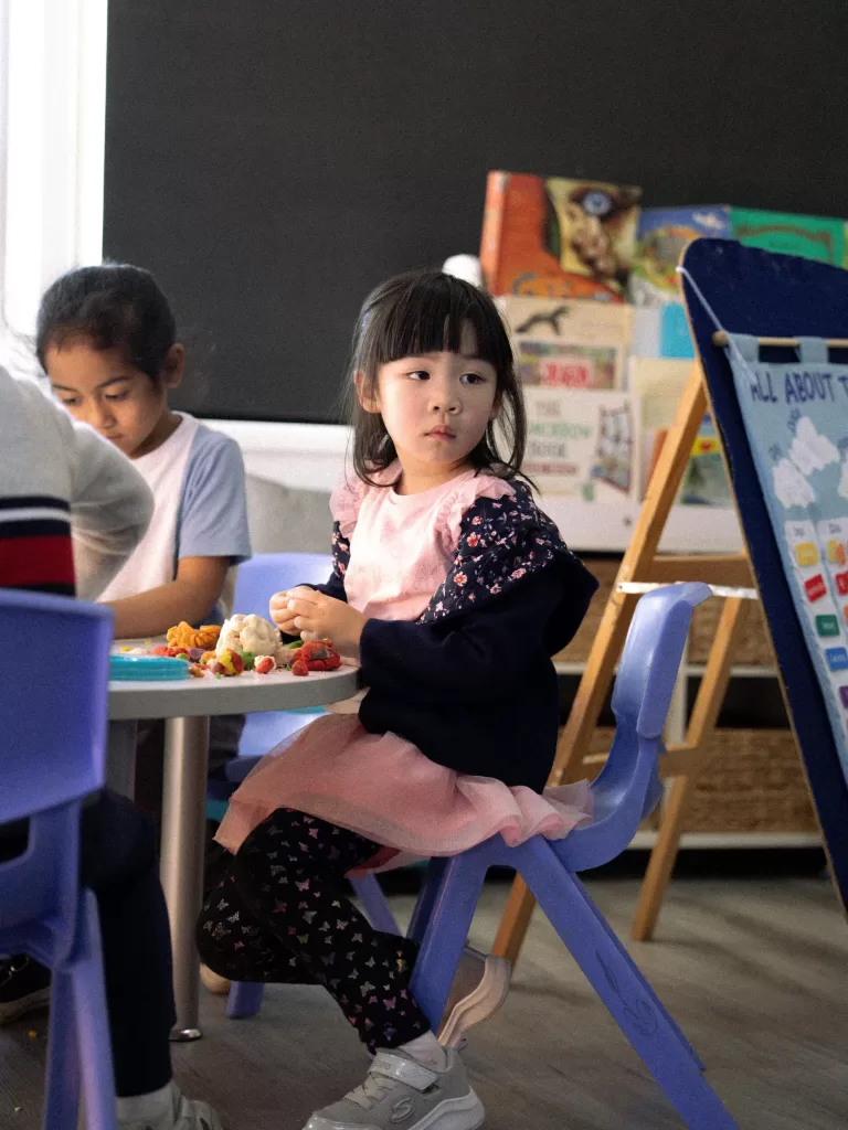 Kinderworld Early Learning Centre child seated at classroom table during meal and playtime with books and learning posters in the background