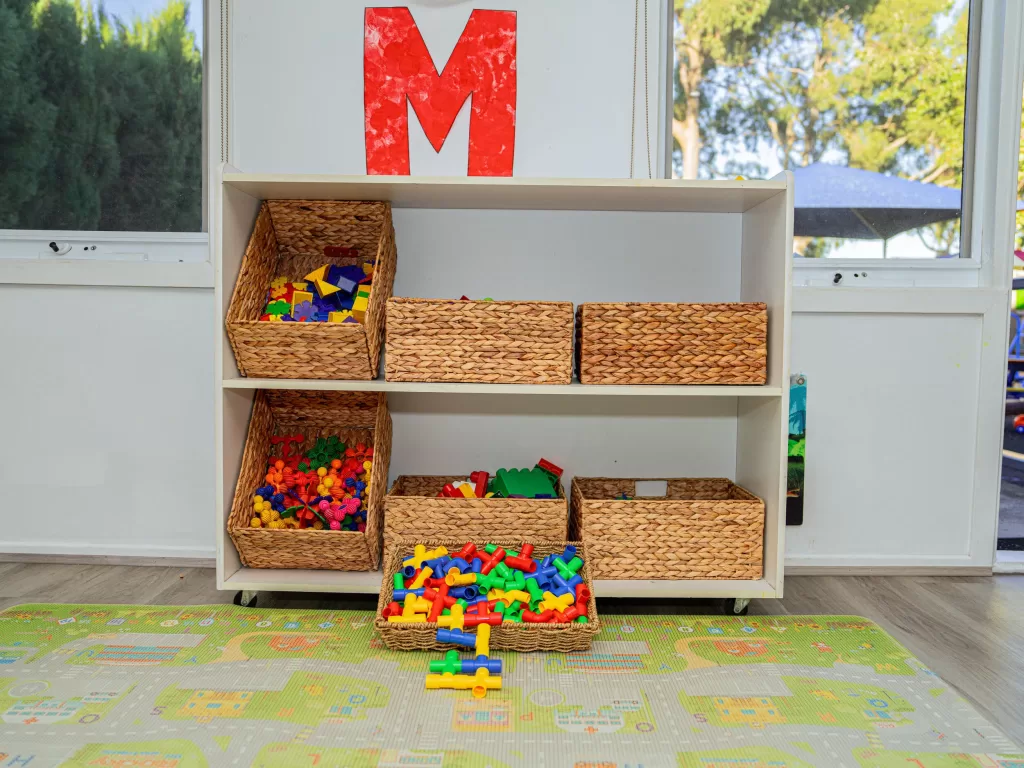 Kinderworld Early Learning Centre indoor activity shelf with labelled wicker baskets and colourful learning blocks for hands-on play
